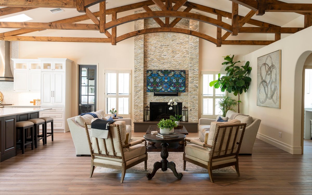 An open living room with timber trusses, a stone fireplace and cream armchairs